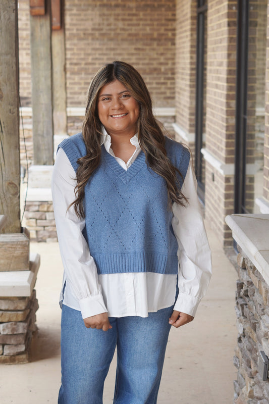 Woman wearing a blue Sweater Vest Top with a white button up underneath the vest paired with jeans
