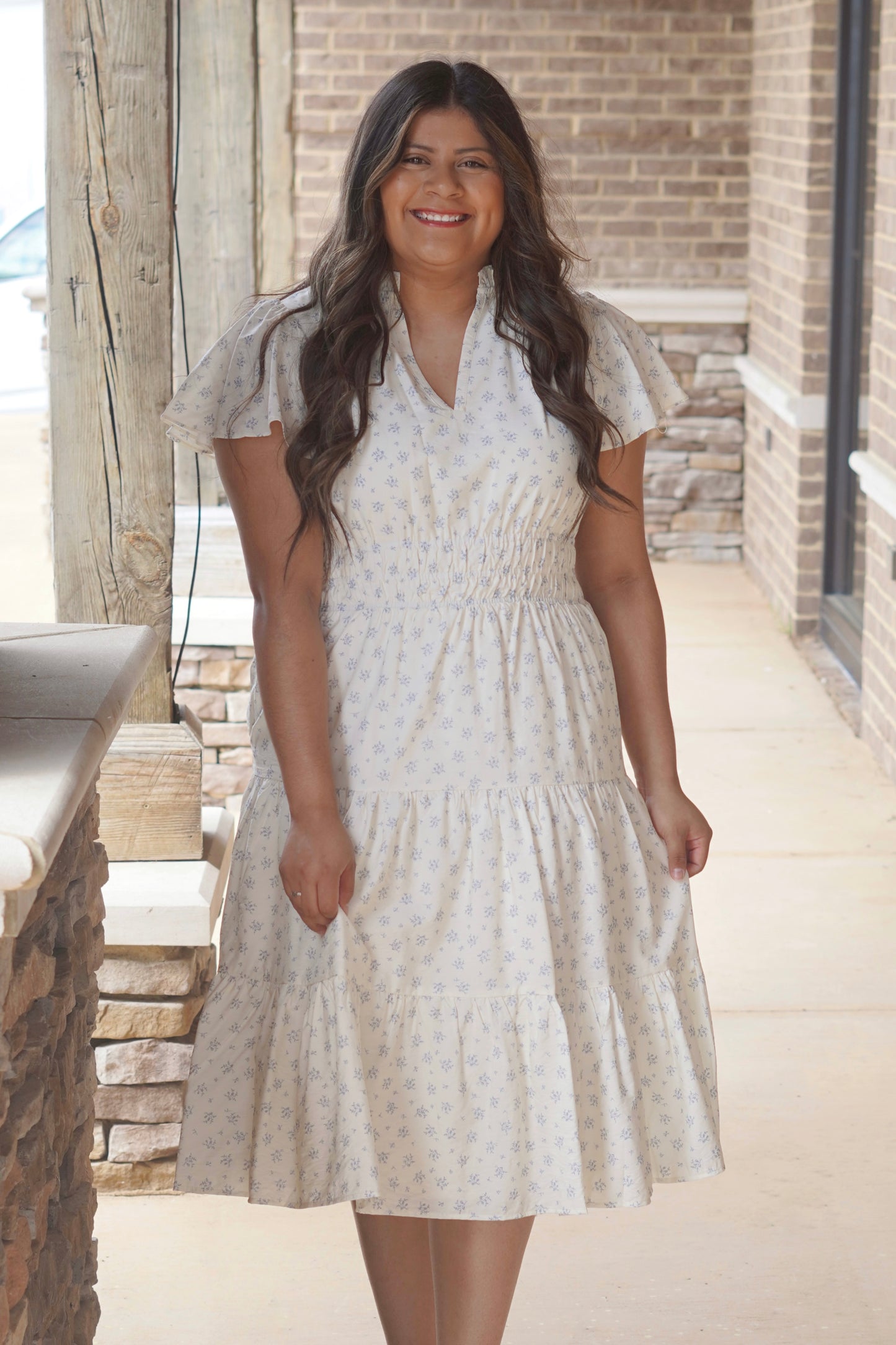 Women wearing a blue floral print midi dress, has a flutter sleeve and a v-neckline, thick elastic band in the waist. 