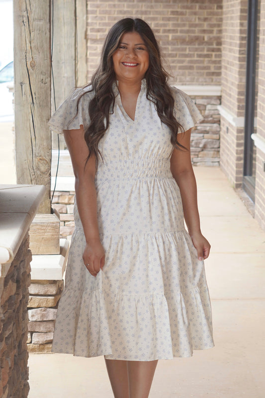Women wearing a blue floral print midi dress, has a flutter sleeve and a v-neckline, thick elastic band in the waist.