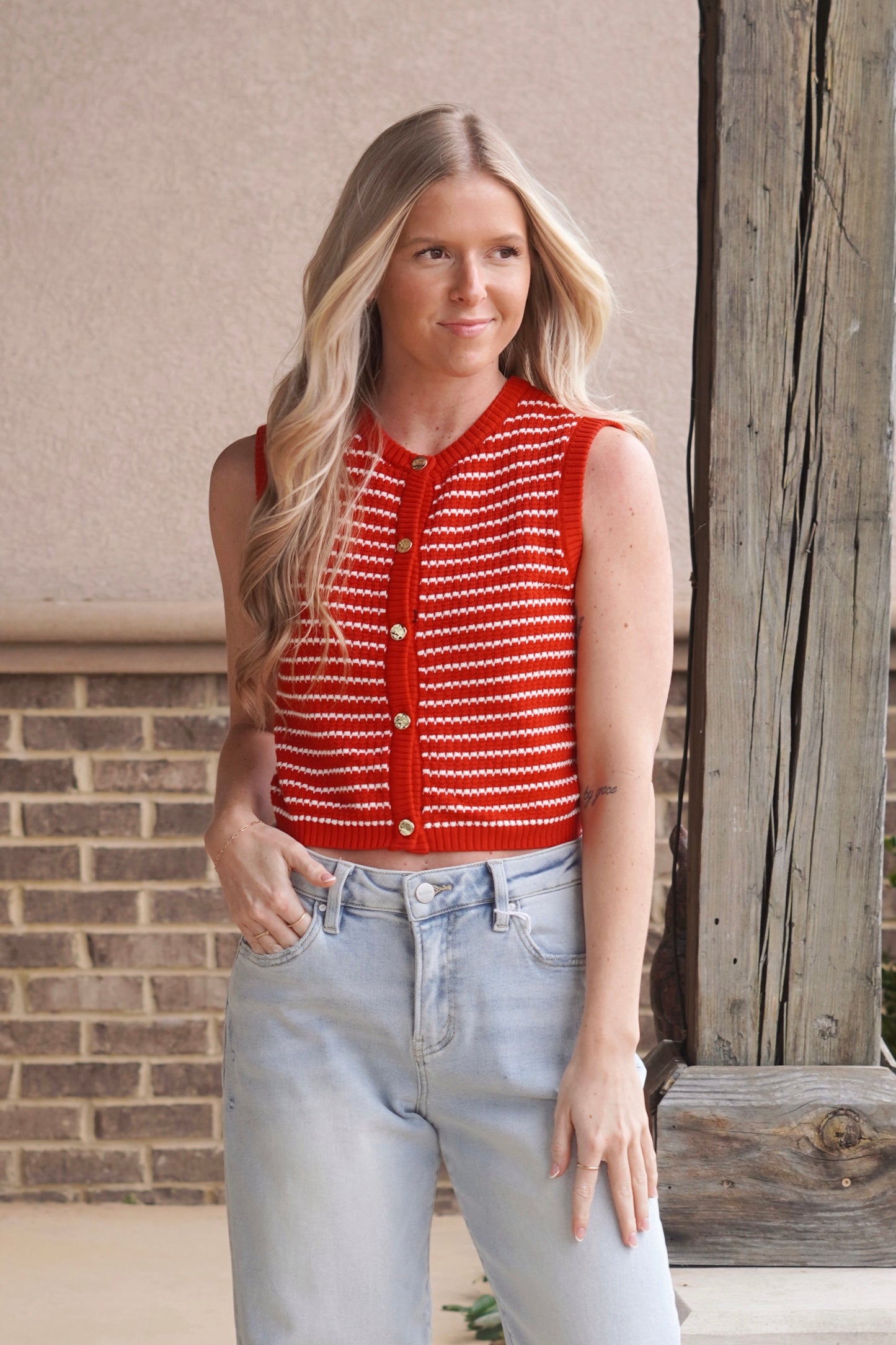 Women wearing a red with white stripes sleeveless knit vest, with gold buttons going down the middle, round neckline. 