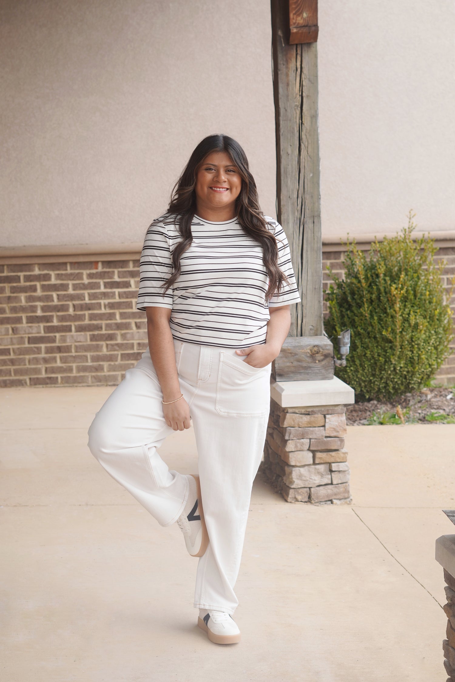 Women wearing a white with black short sleeve t shirt, round neckline, ribbed material, paired with some white jeans 