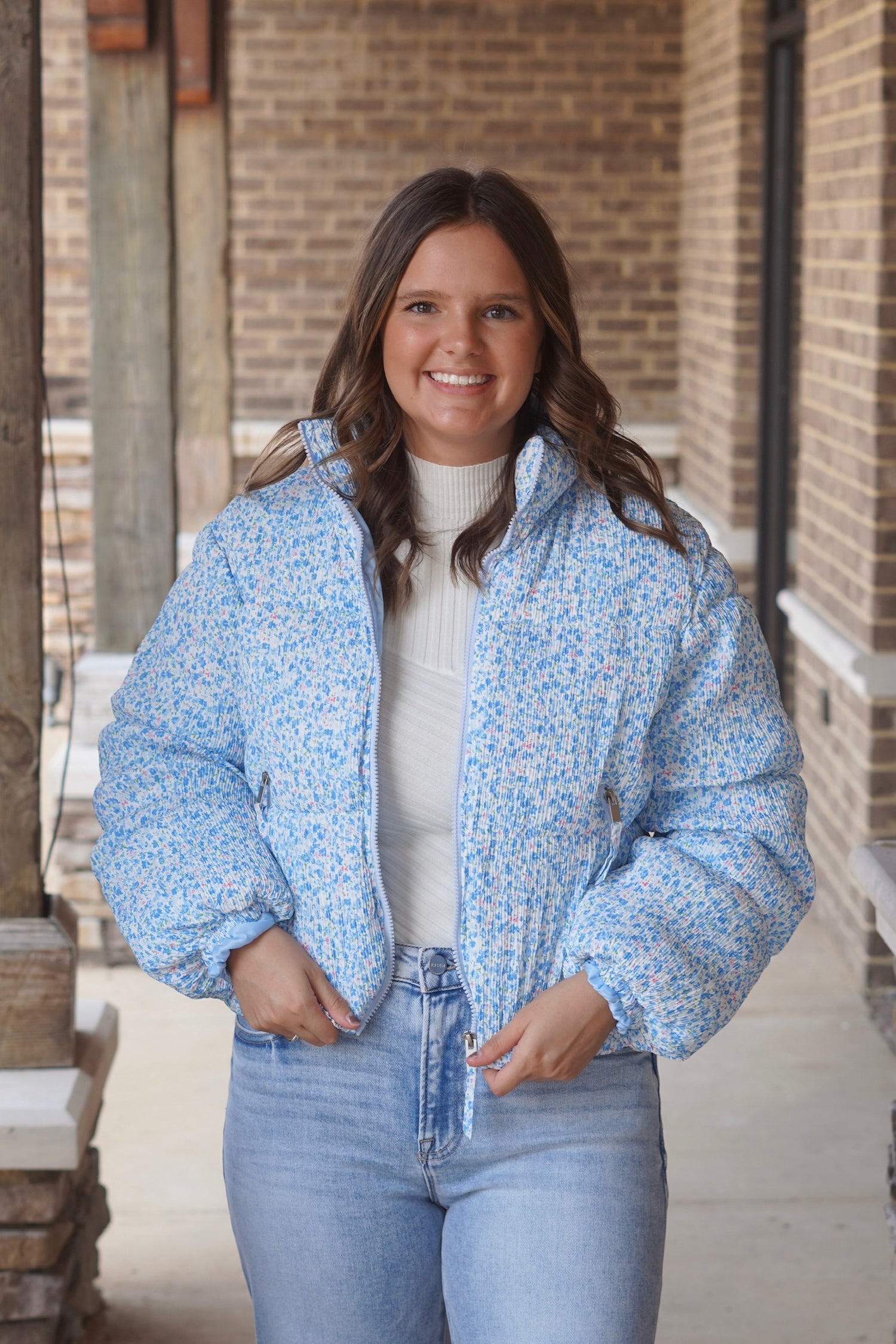 Woman wearing a blue floral printed cropped puffer jacket with a white fitted top underneath and paired with. jeans