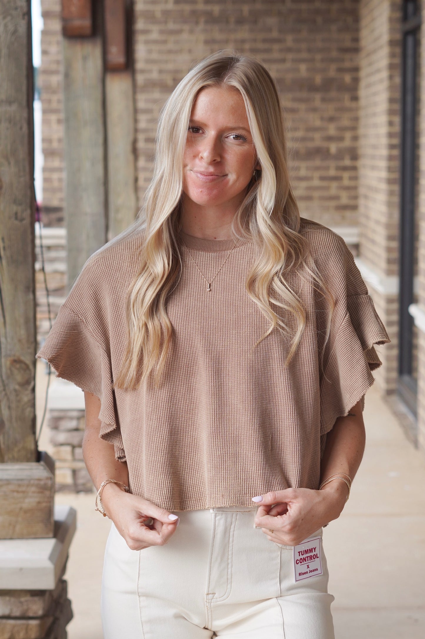 Woman wearing a brown short ruffle sleeve waffle knit top paired with cream colored jeans 