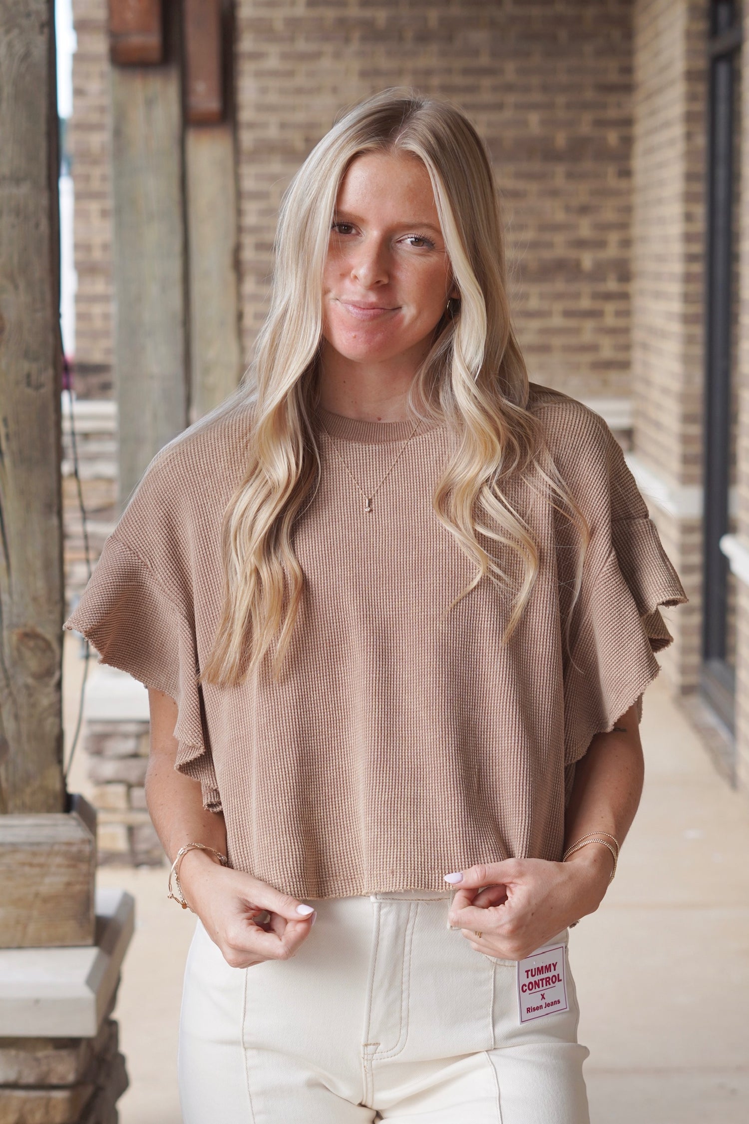 Woman wearing a brown short ruffle sleeve waffle knit top paired with cream colored jeans 