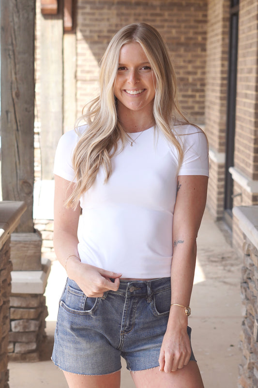 Women wearing a white fitted short sleeve top, round neckline paired with jean shorts.
