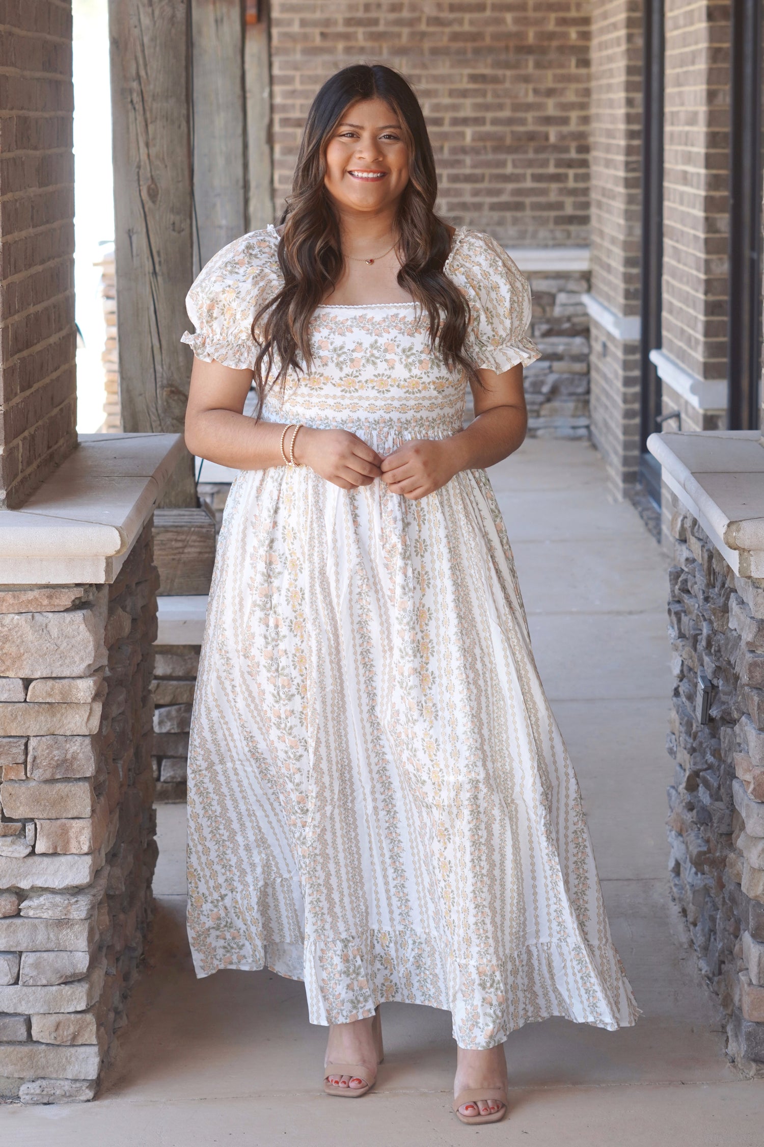 A women wearing a yellow and white maxi dress with a floral pattern, puff sleeves, and a square neckline.