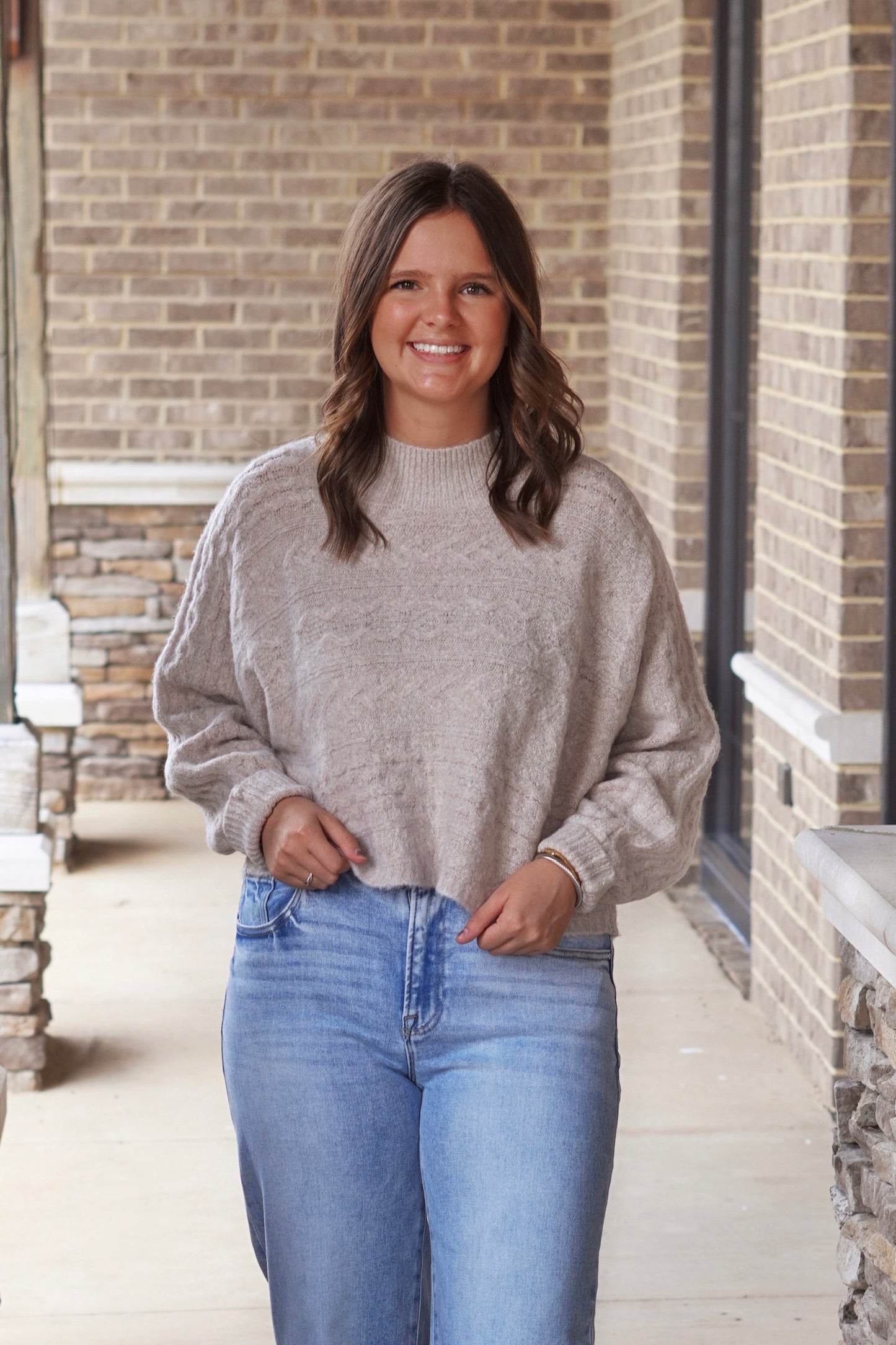 Woman wearing cropped mock neck sweater in the color oat paired with light wash jeans