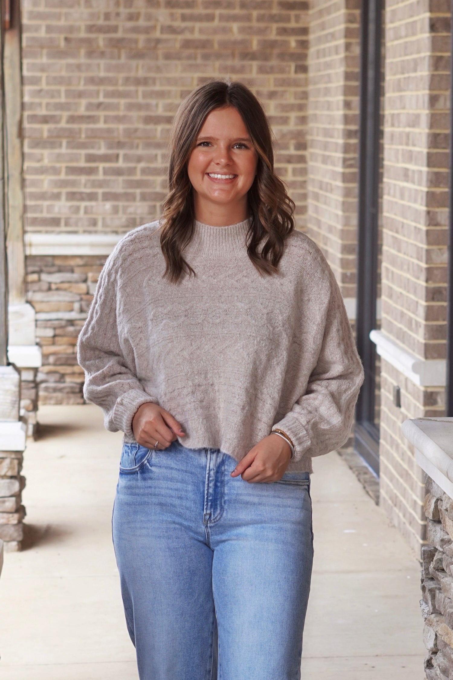Woman wearing cropped mock neck sweater in the color oat paired with light wash jeans