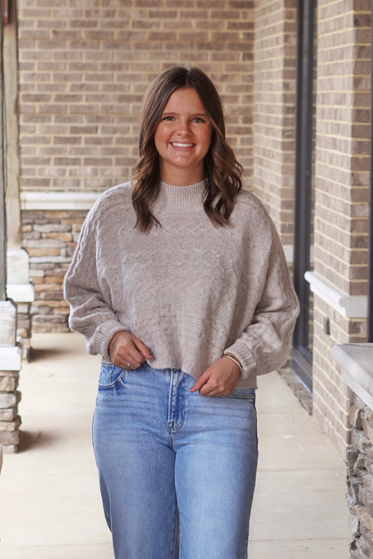 Woman wearing cropped mock neck sweater in the color oat paired with light wash jeans