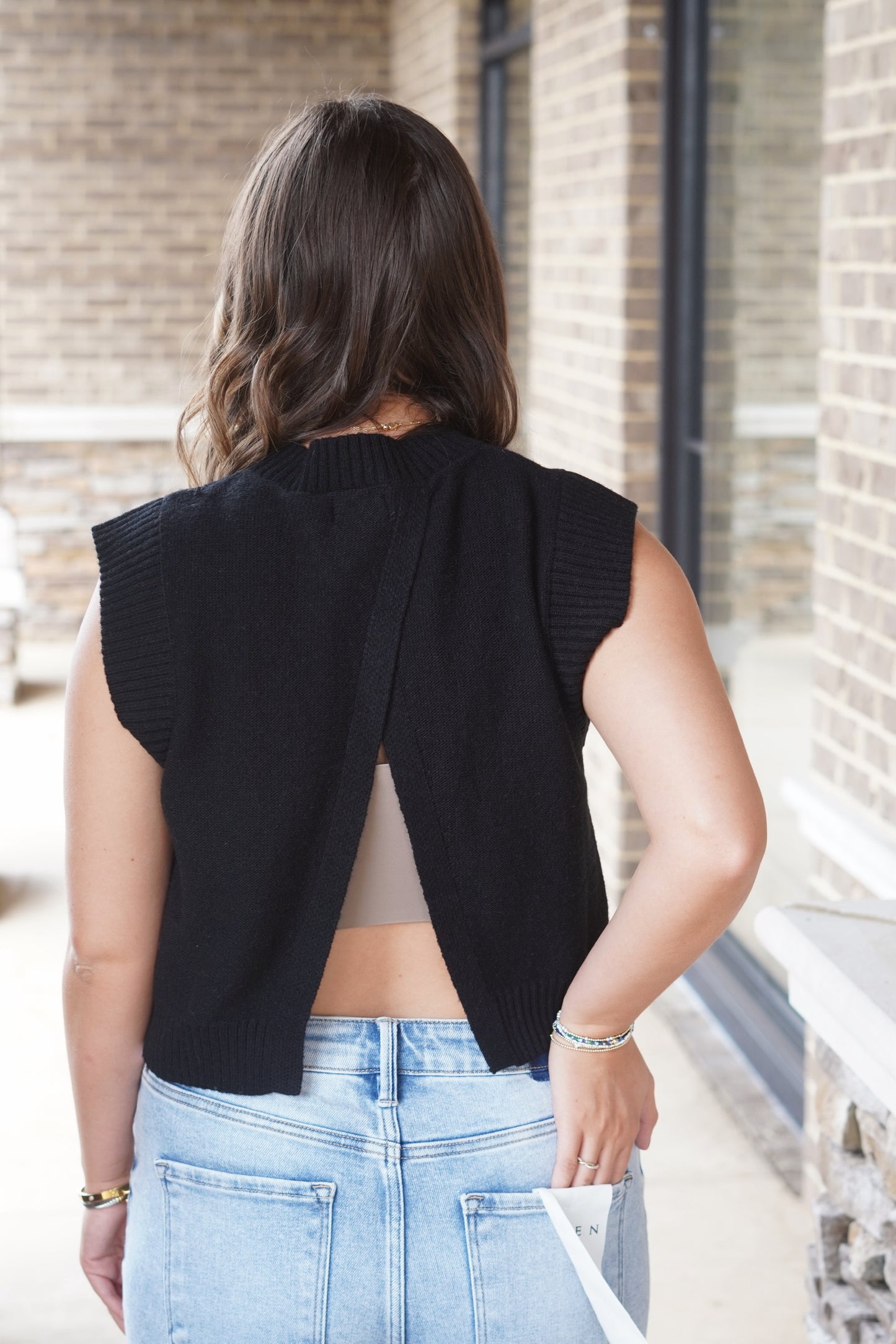 Woman wearing a black cropped relaxed fit sleeveless top with an open back paired with jeans 