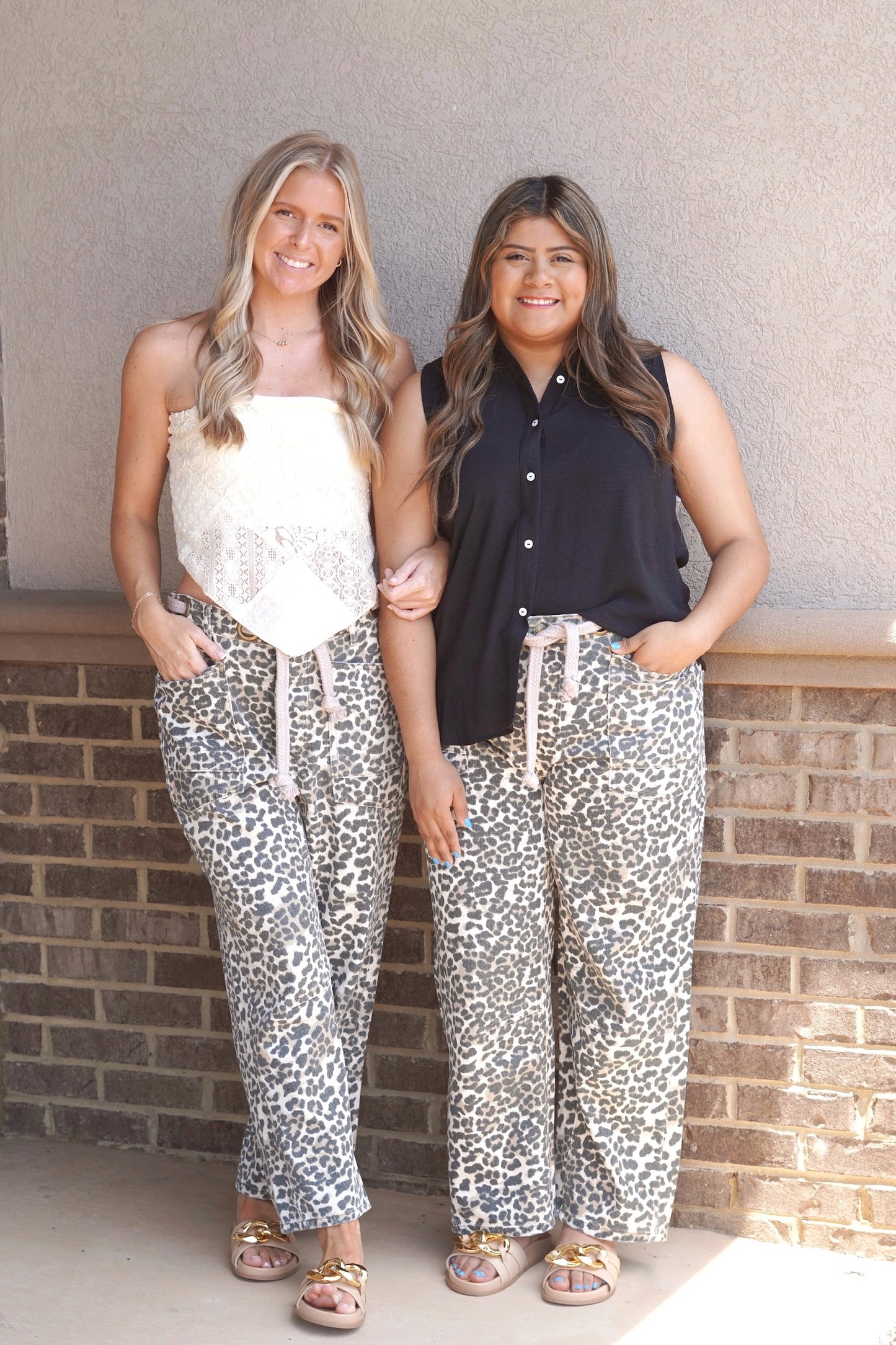 Two women wearing Leopard print wide legged jeans. Belt included with jeans that is rope like material. Front and back pockets. Gold metal hoops serving as belt loops. 