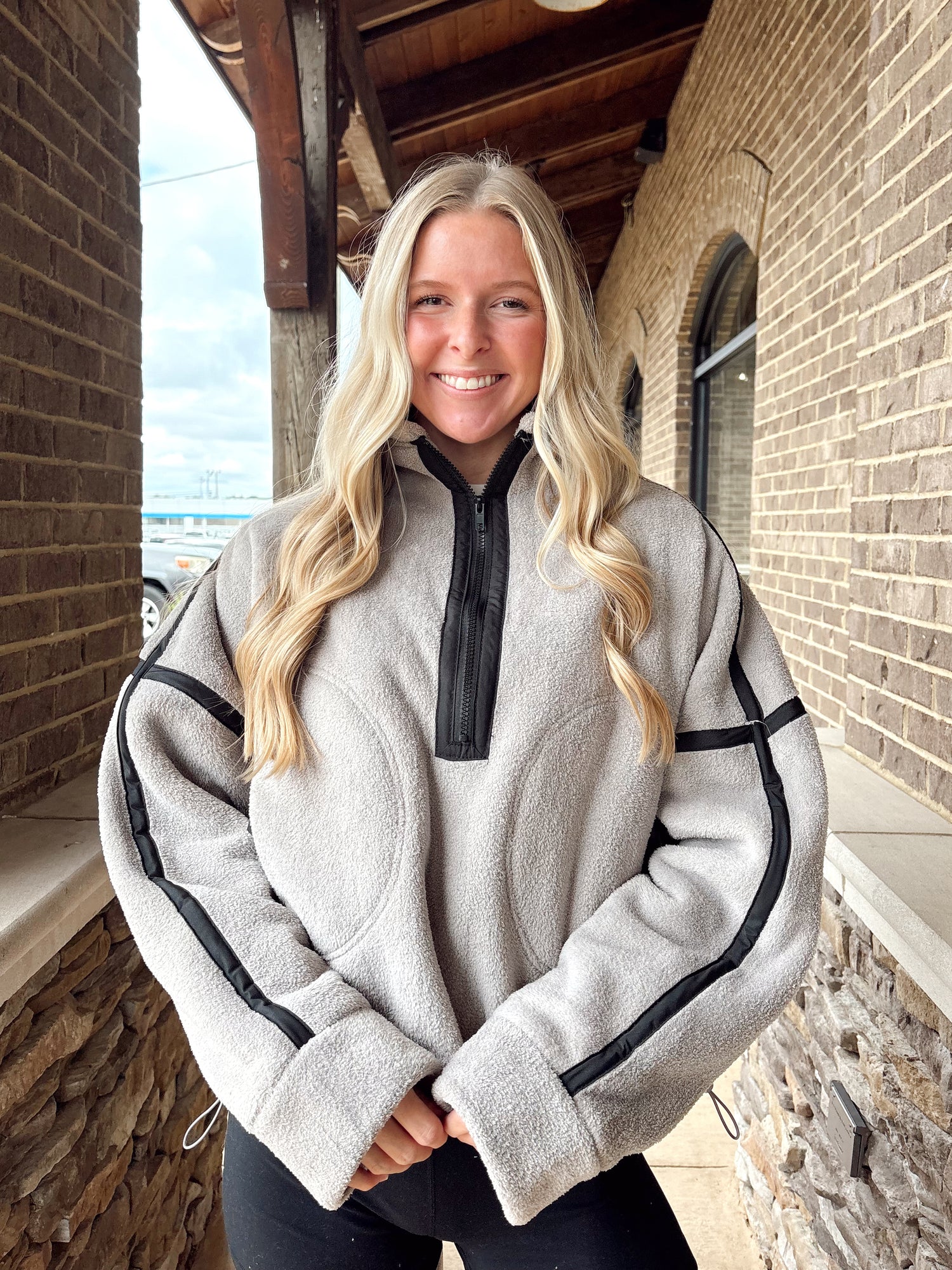 Woman wearing a grey-colored fleece quarter-zip pullover with black stripe details on the sleeves, paired with black athletic shorts.