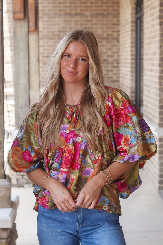 Woman wearing a floral printed short puff sleeve top with a tie in the front paired with dark wash jeans