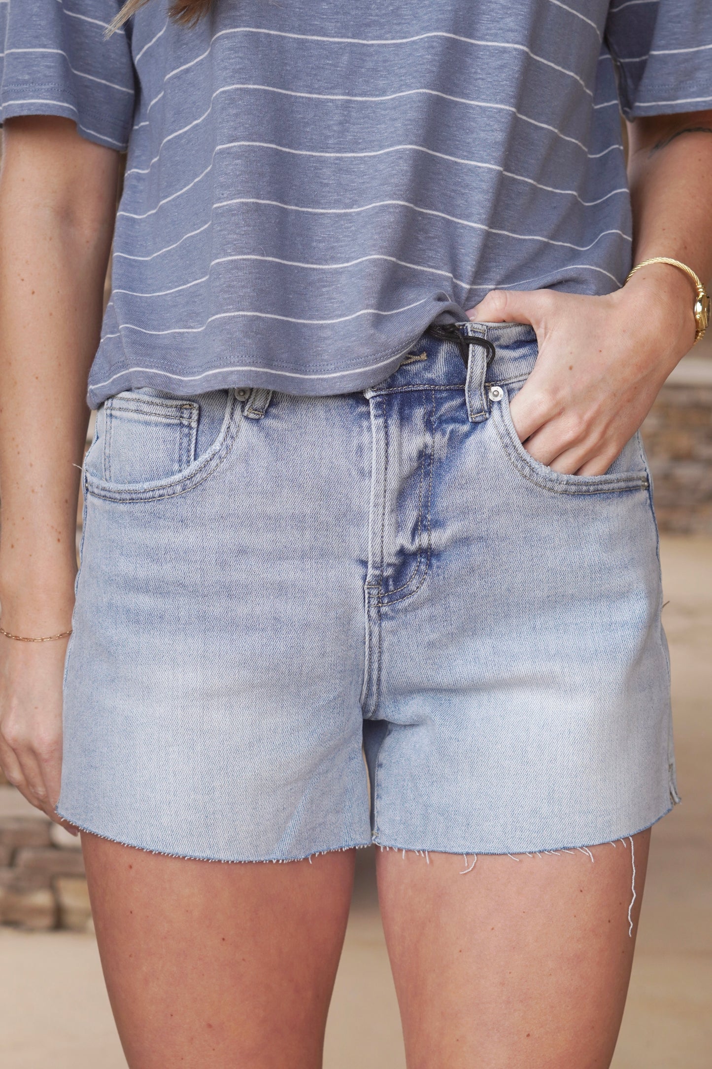 Woman wearing light wash blue jean shorts with raw hem and pockets paired with a blue and white striped top