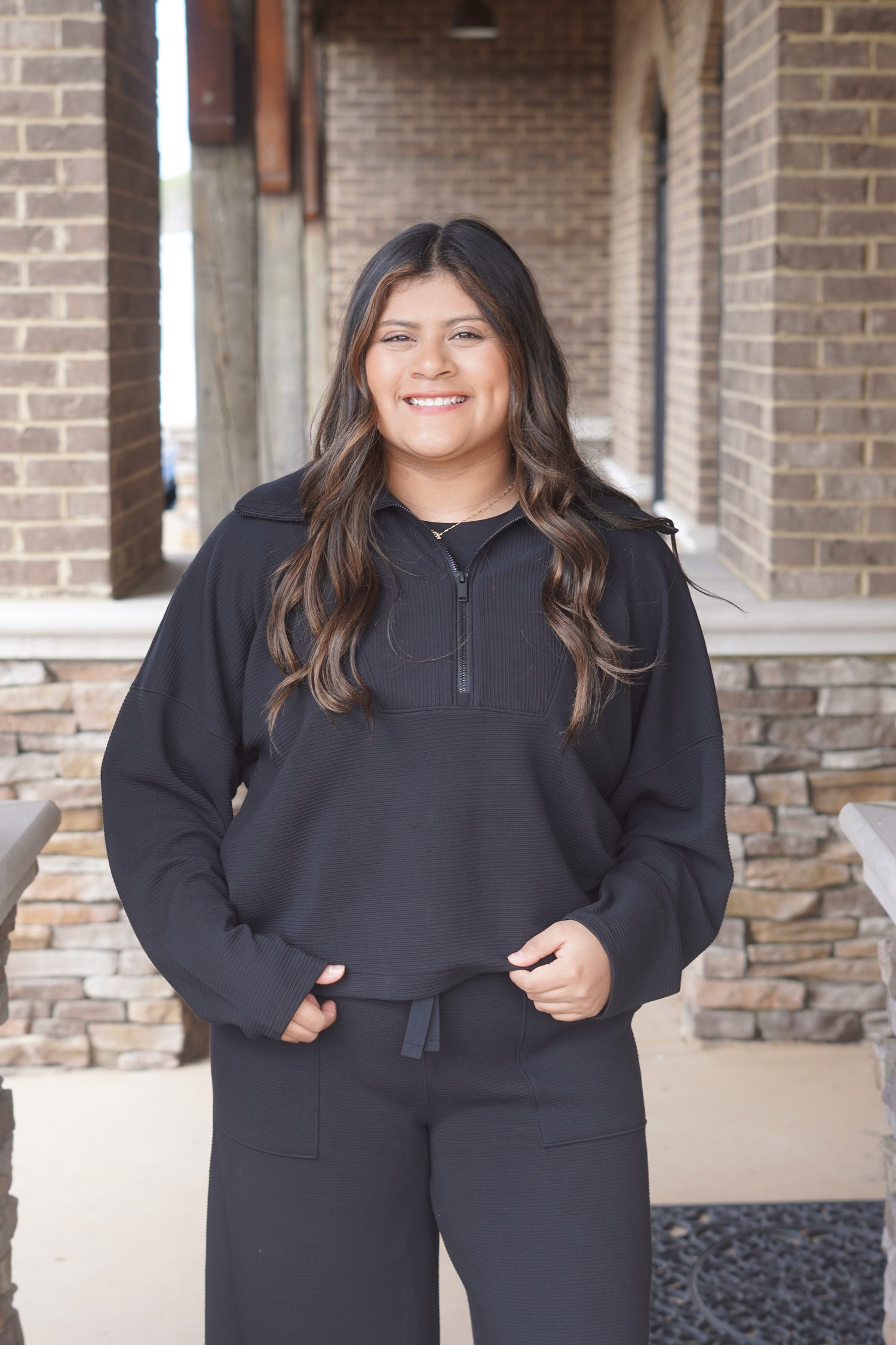 Woman wearing a black, long sleeve, ribbed, half zip top paired with matching pants