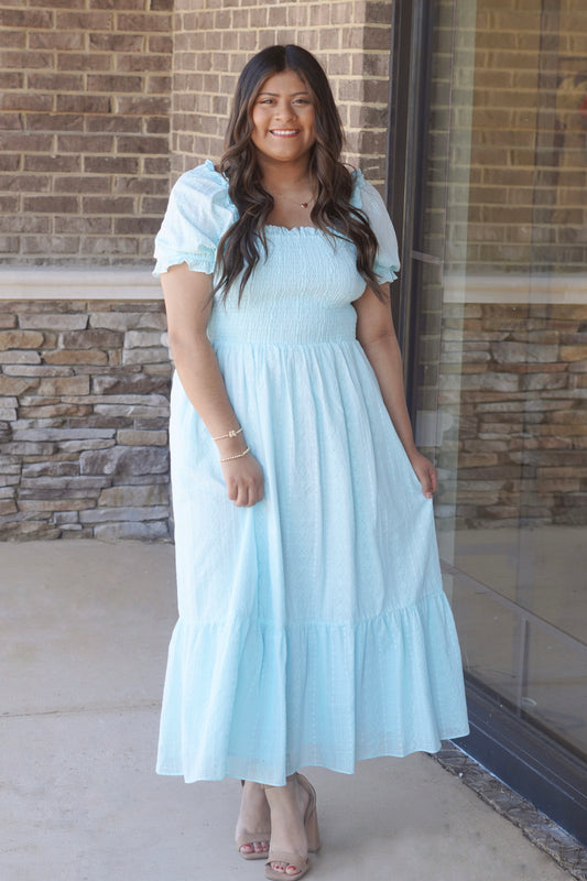 Woman wearing a square neck, light blue, maxi dress with puff sleeves paired with heels.