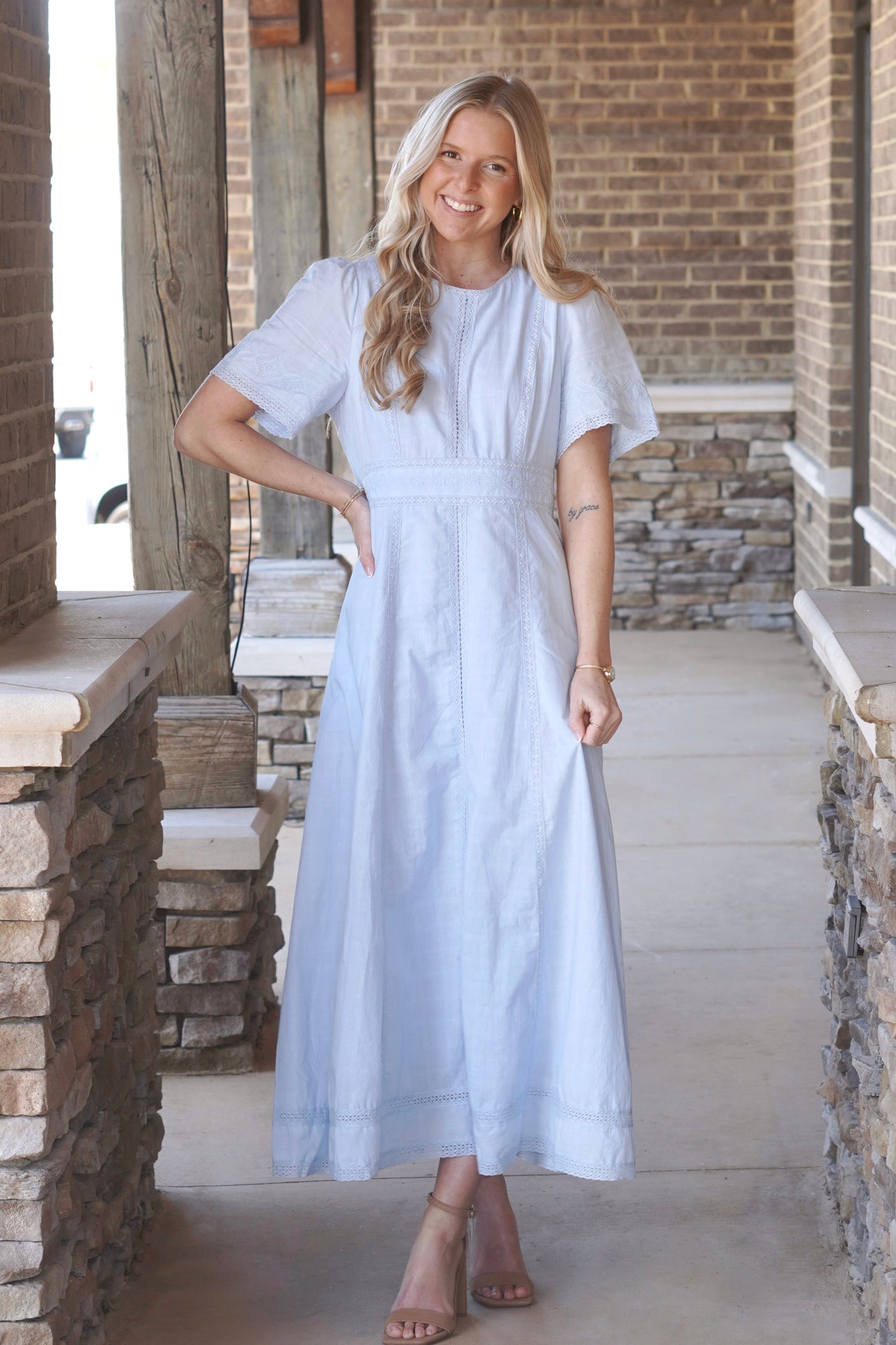Women wearing a light blue, short sleeve, maxi dress, that have lace detailing and a round high neckline, paired with nude heels.