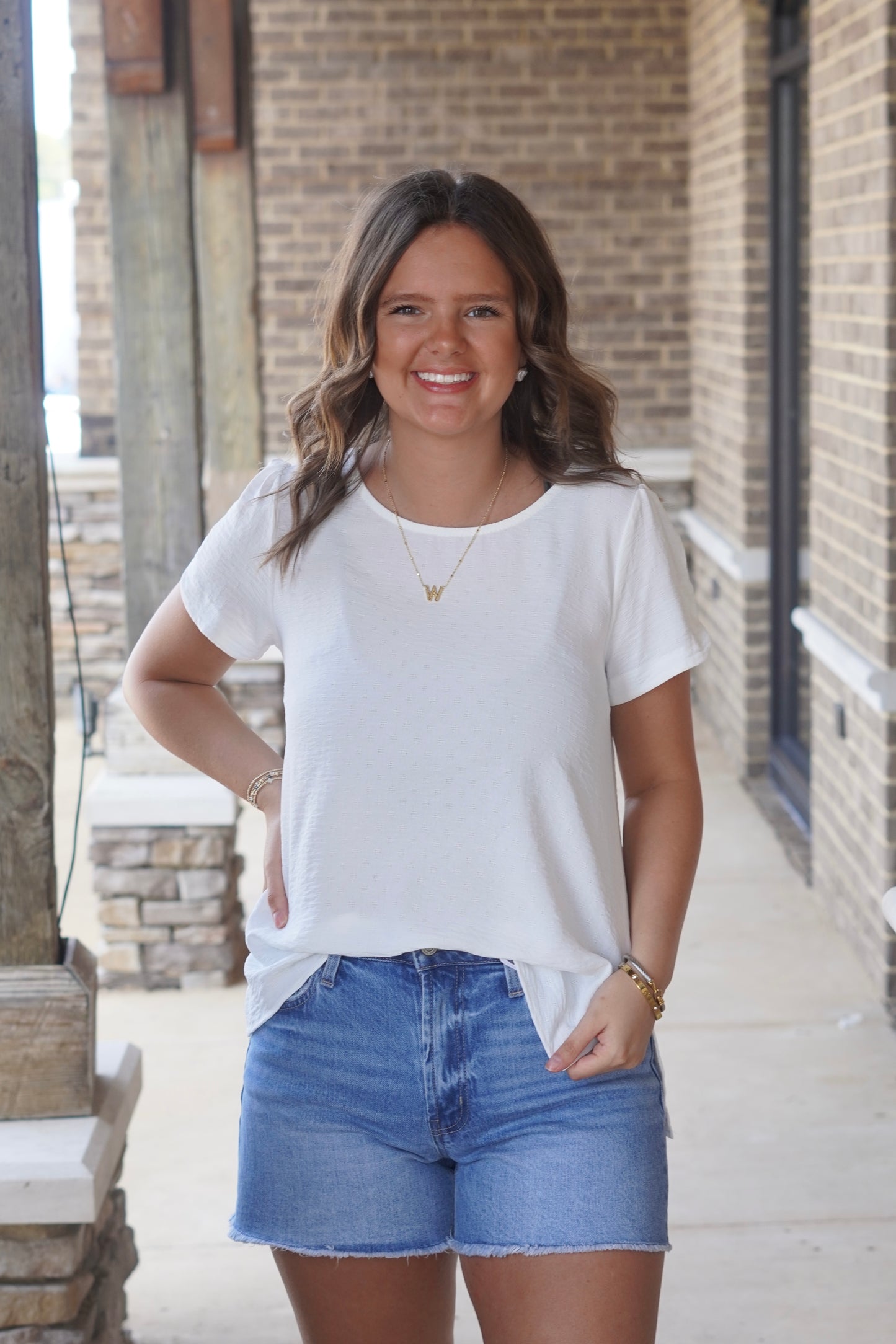 Women wearing a white blouse, short sleeve, flowy, with some textured, paired with blue jean short. 
