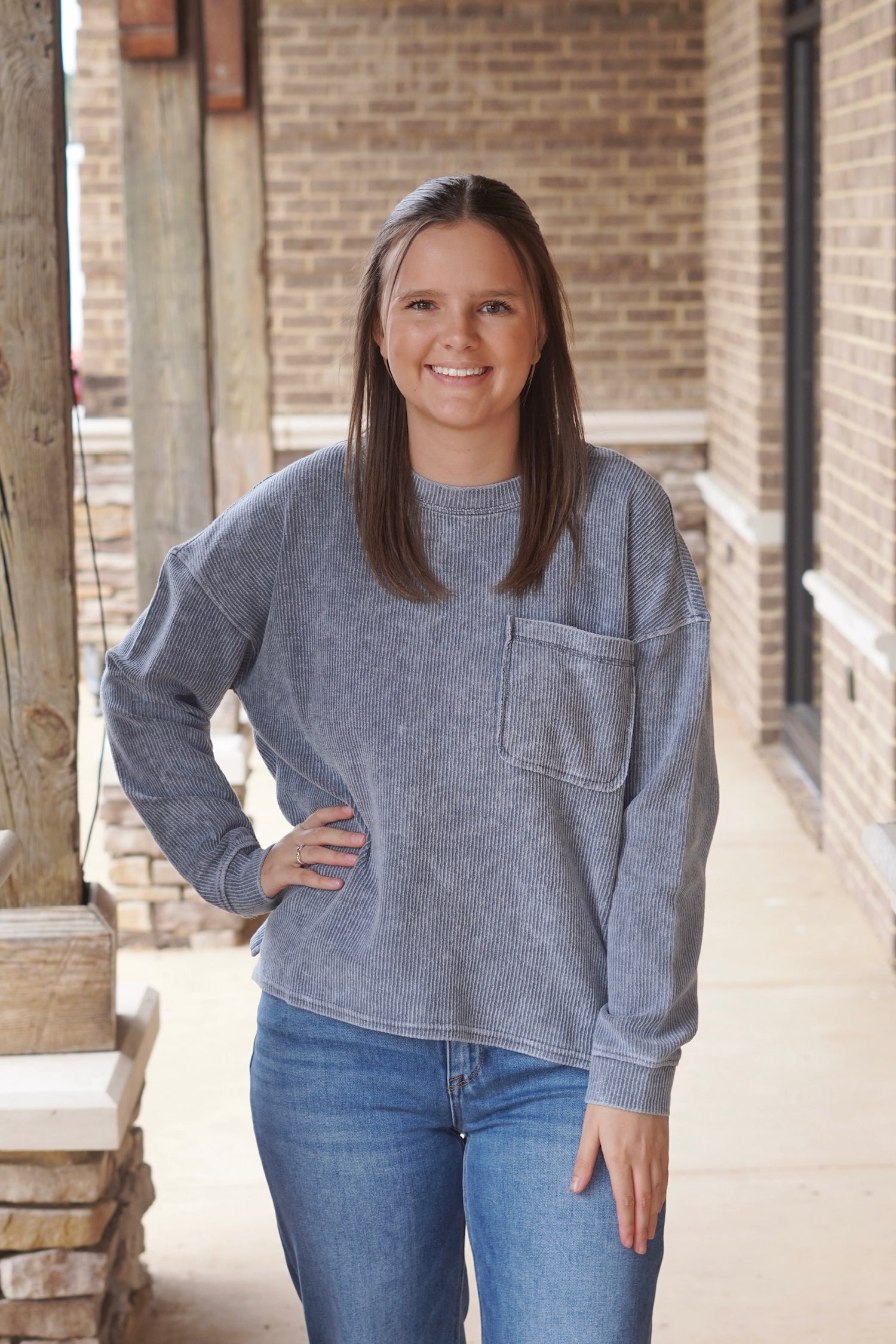 Woman wearing a denim colored corned sweatshirt with a front pocket pair with denim jeans