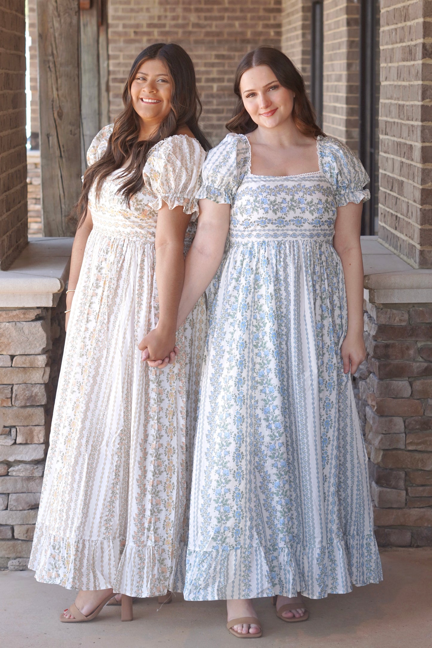 Two women wearing blue and yellow maxi dresses with a floral pattern, puff sleeves, and a square neckline.