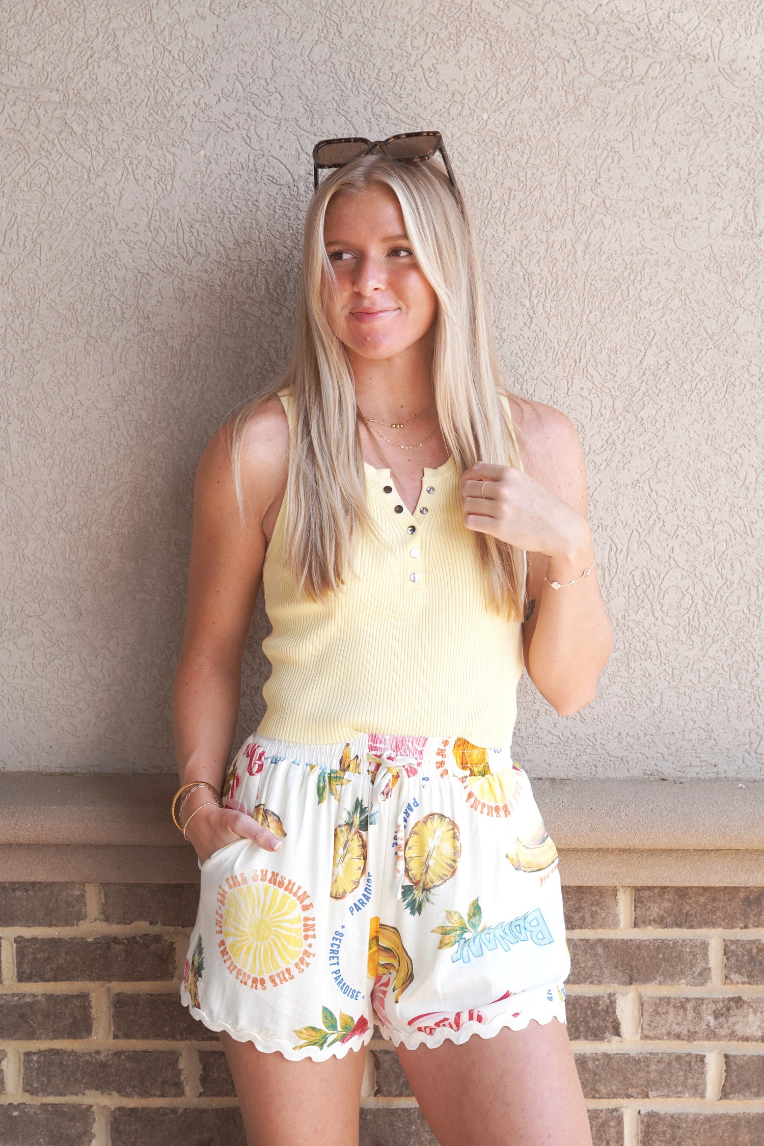 Women wearing white shorts with fruit print paired with a yellow tank top 