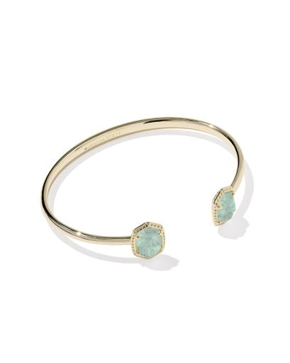 Gold open cuff bracelet with teal  stone at the end in a gold texture frame. 