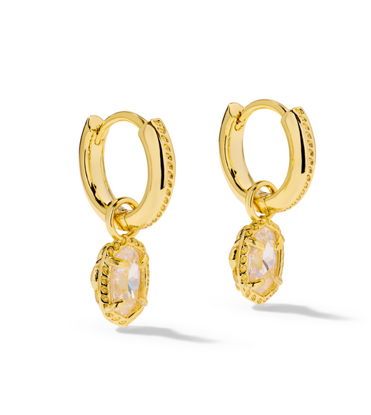 A pair of gold huggie hoop earrings with dangling textured bezel settings holding oval clear gemstones.