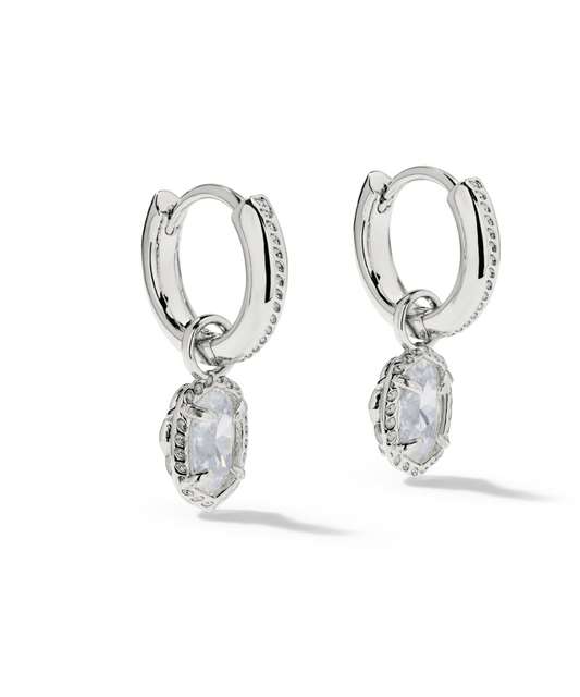 A pair of silver huggie hoop earrings with dangling oval clear gemstones.