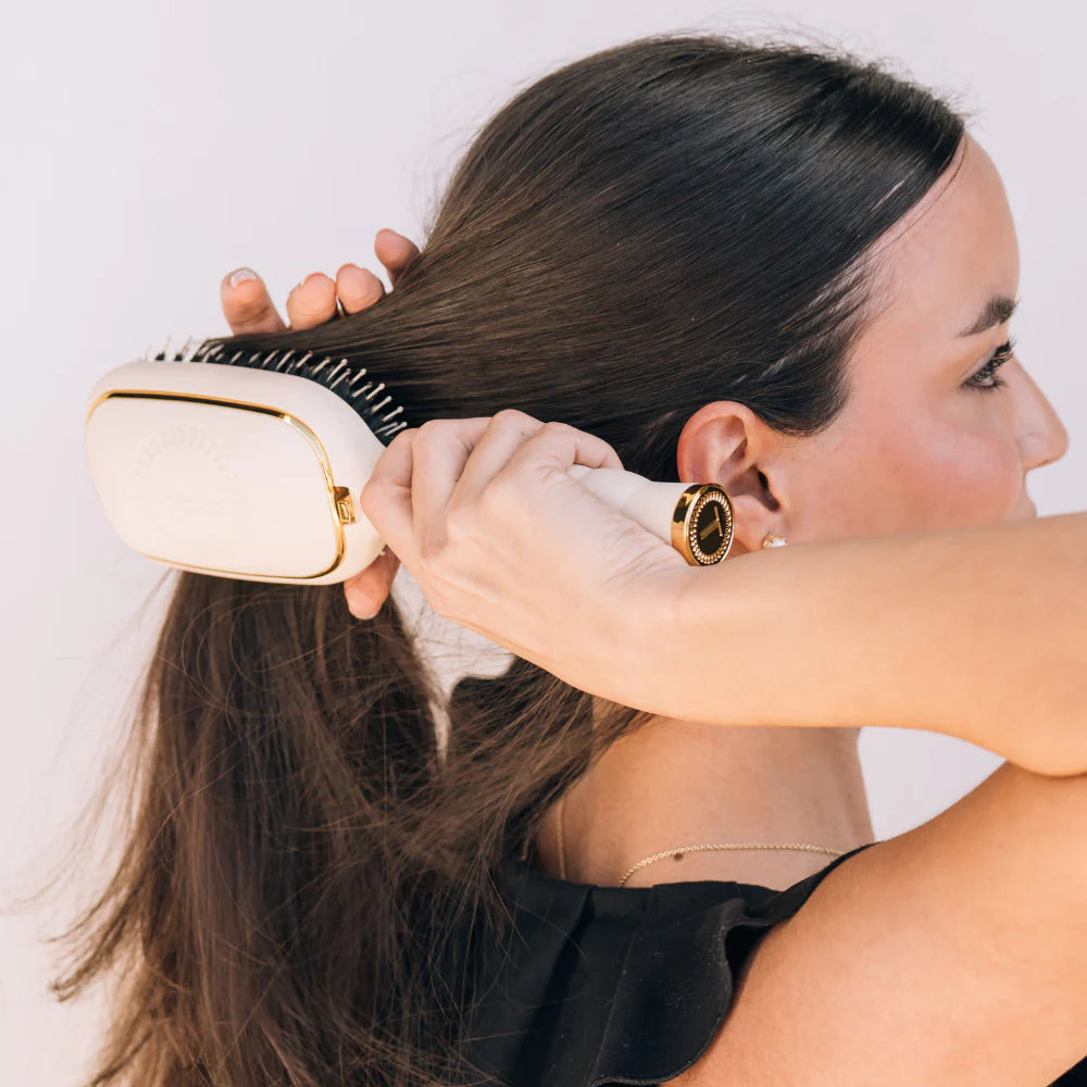 Woman brushing long dark hair with oval hair brush, beige handle, boar bristle, textured handle with gold trim