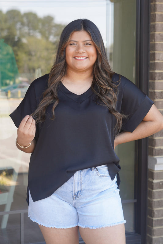 Woman wearing a black v-neck top, short sleeve, flowy, paired with light blue jean shorts