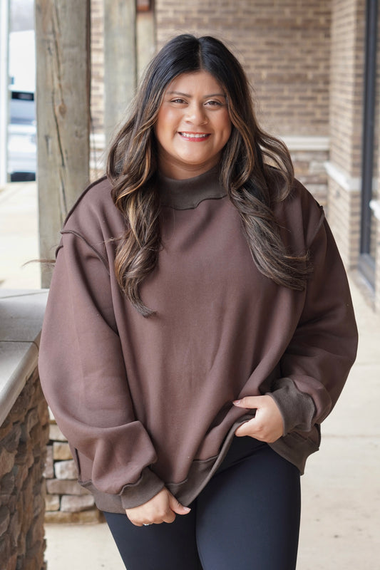 Woman wearing a brown oversized mock neck sweatshirt with black leggings. 