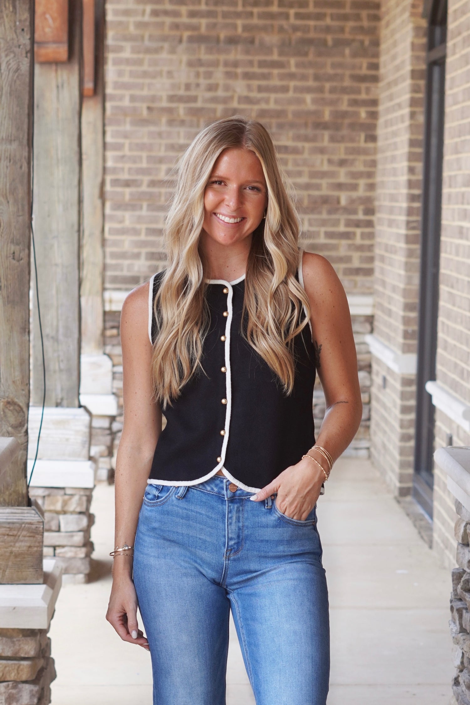 Women wearing a black sleeveless button up top with a white outline paired with light wash blue jeans