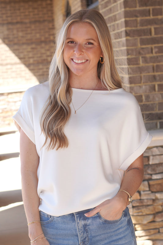 Woman wearing a short sleeve white top with a round neckline and rolled sleeves paired with blue jeans