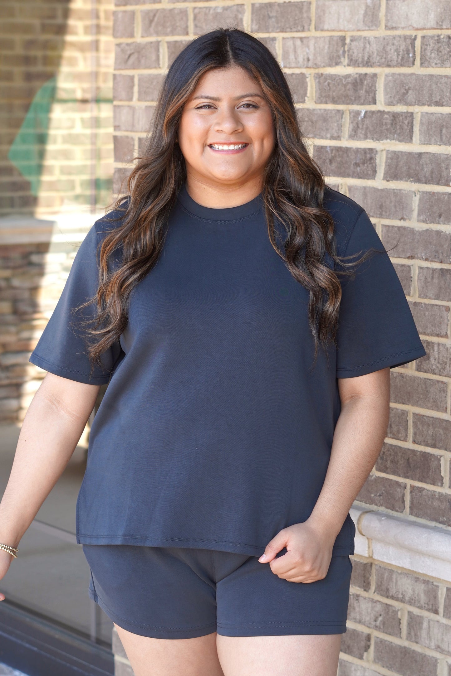 Woman wearing a black oversized short-sleeve tee with side slits, crew neckline, paired with matching black shorts. 