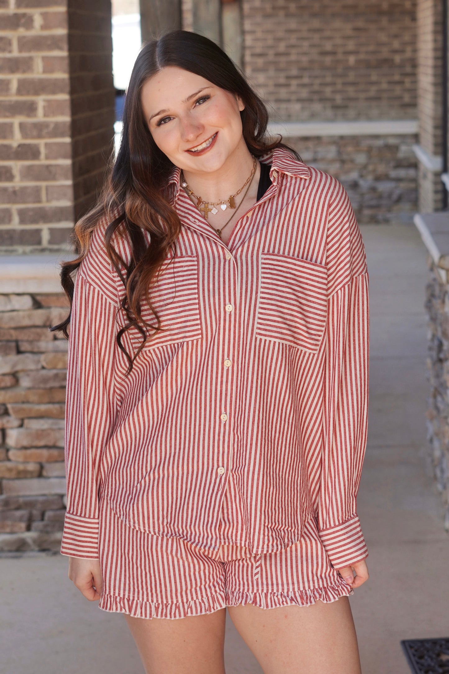 Women wearing a red stripes long sleeve button up top, has pockets, paired with the matching shorts. 