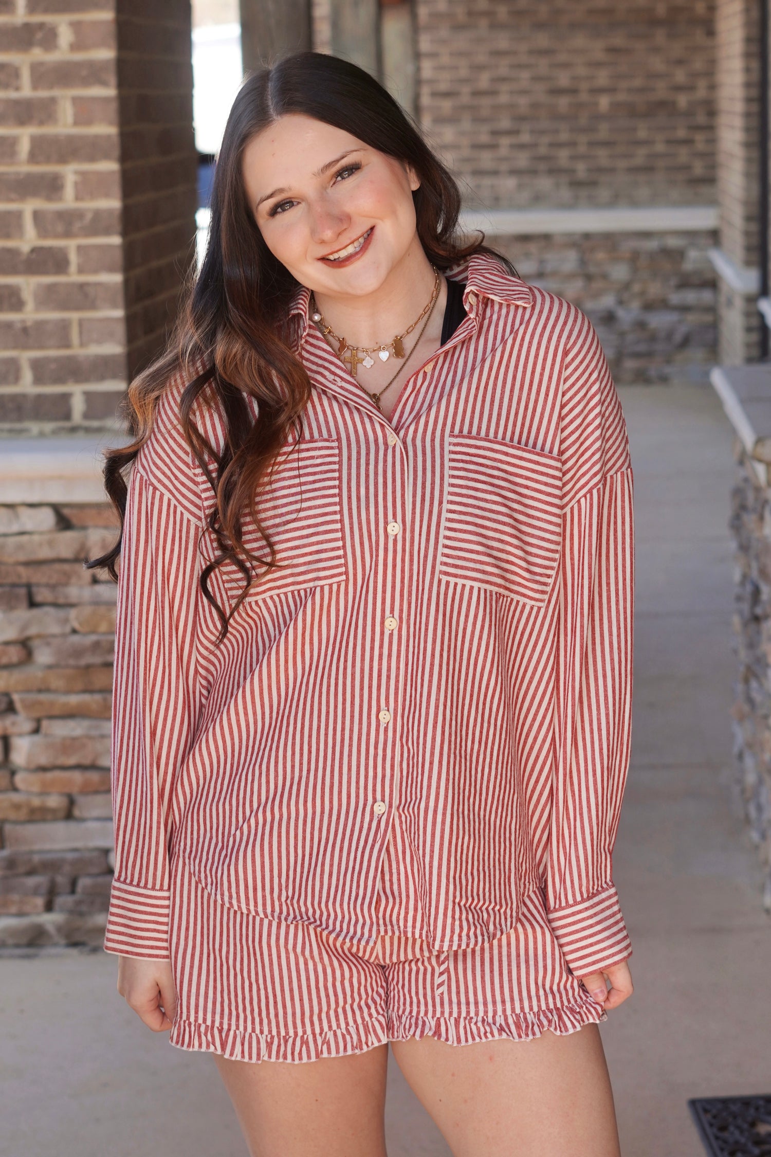 Women wearing a red stripes long sleeve button up top, has pockets, paired with the matching shorts. 