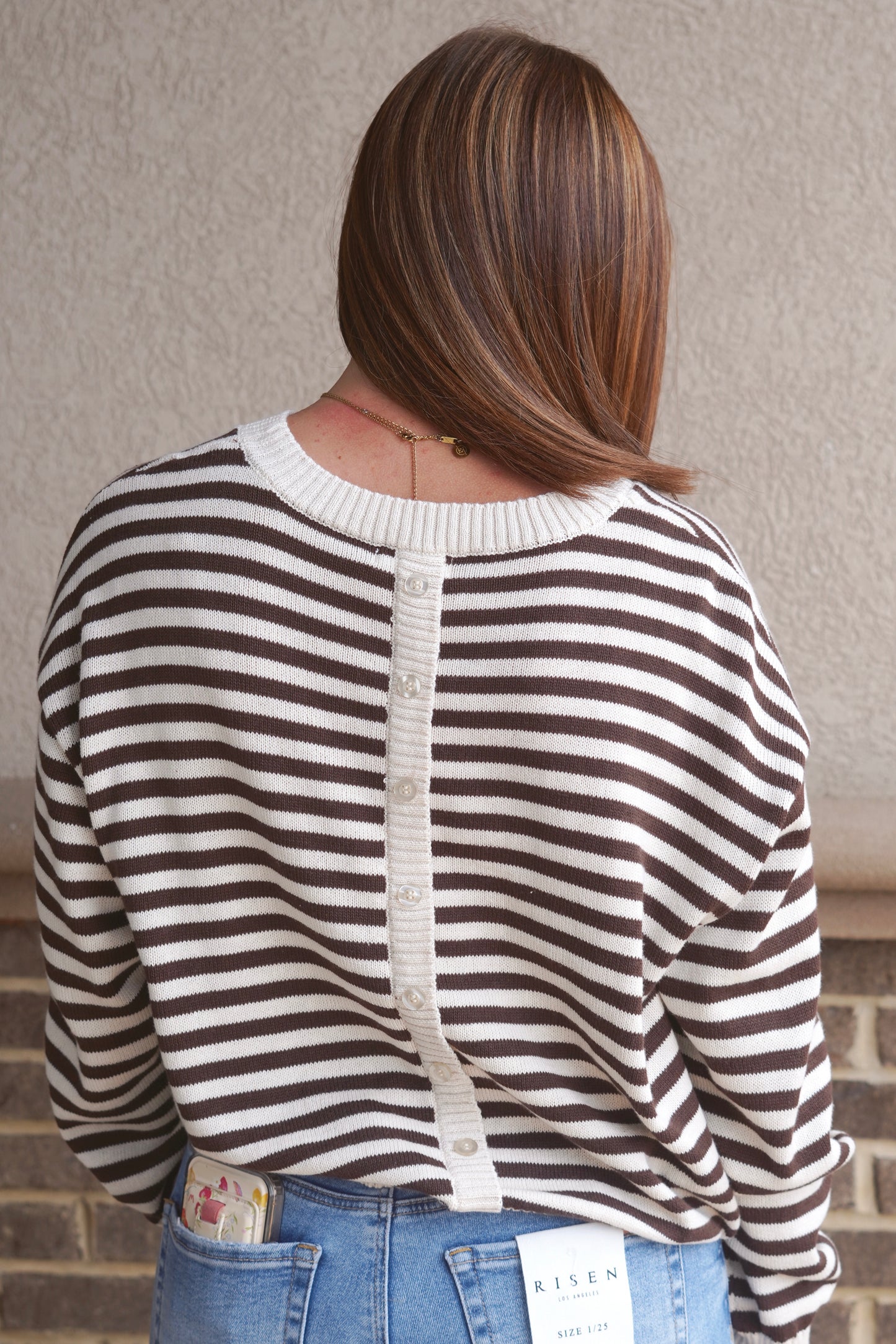 Women wearing a cream and brown striped sweater, crew neckline, button down detail in the back of the sweater. 