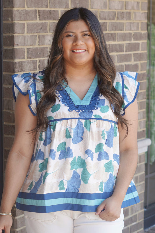 Women wearing a blue floral print top with  a blue outline detail in the bottom, flutter sleeves and a v-neckline. 