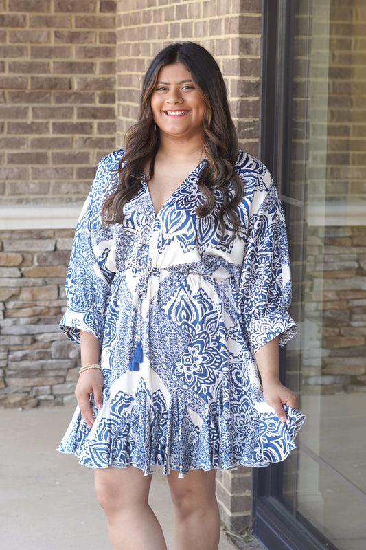 Women wearing a blue pattern dress with a v neckline, mid arm length sleeves, and drawstring waist, above knee length.