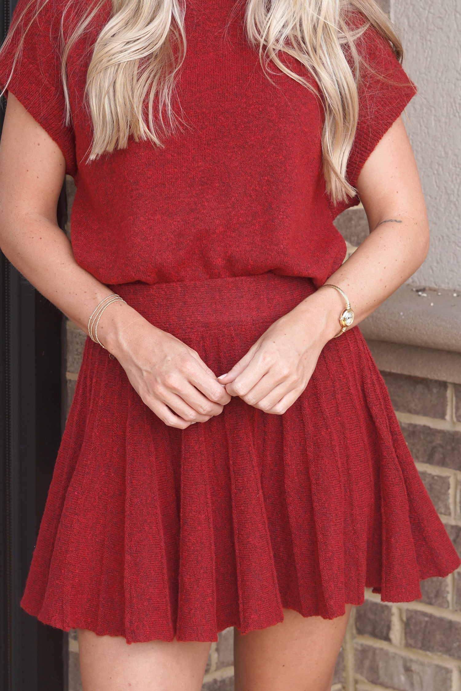 A woman wearing a textured red short-sleeve top and matching pleated red mini skirt. 