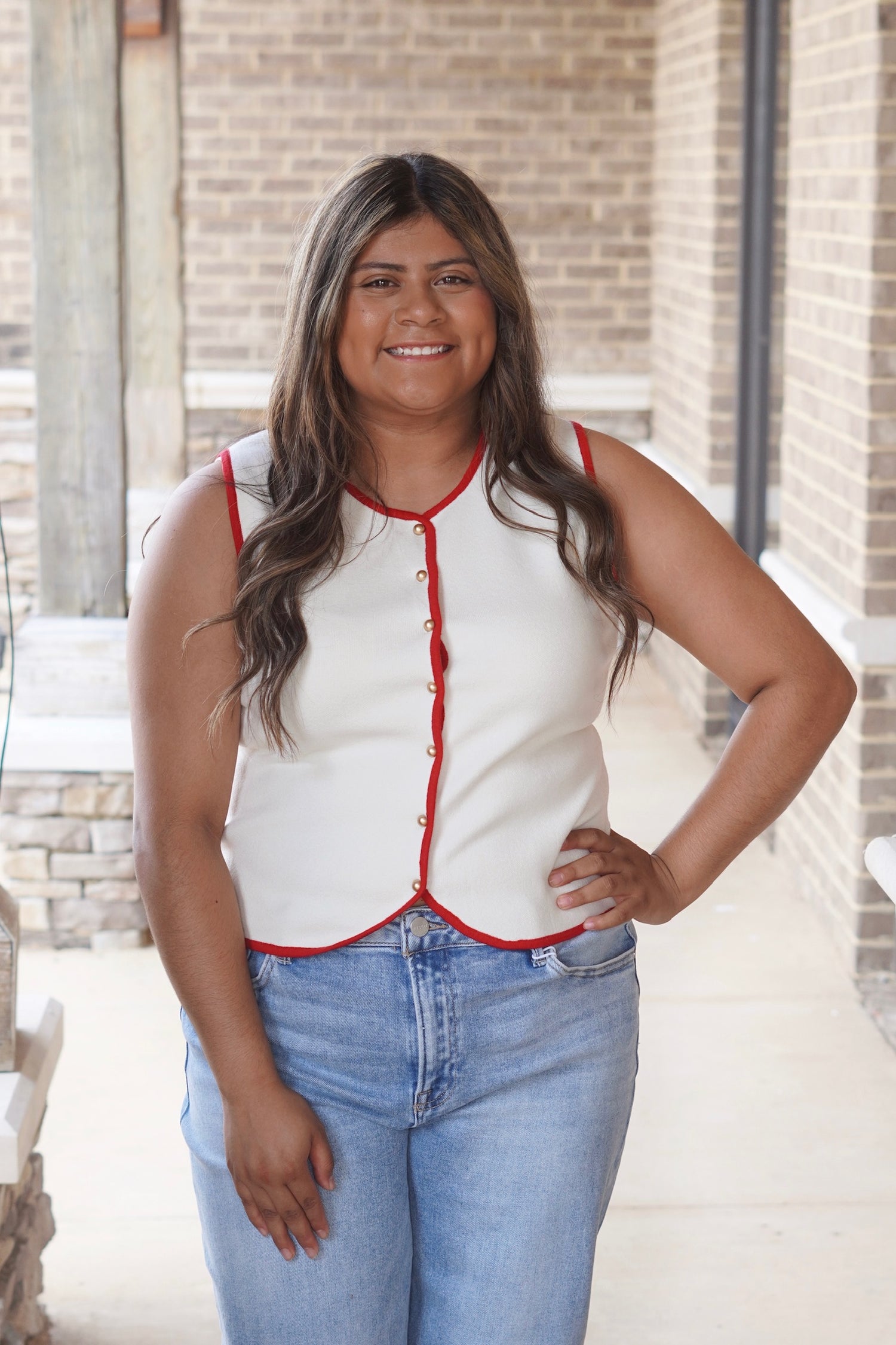 Women wearing a cream sleeveless button up top with a red outline paired with light wash blue jeans