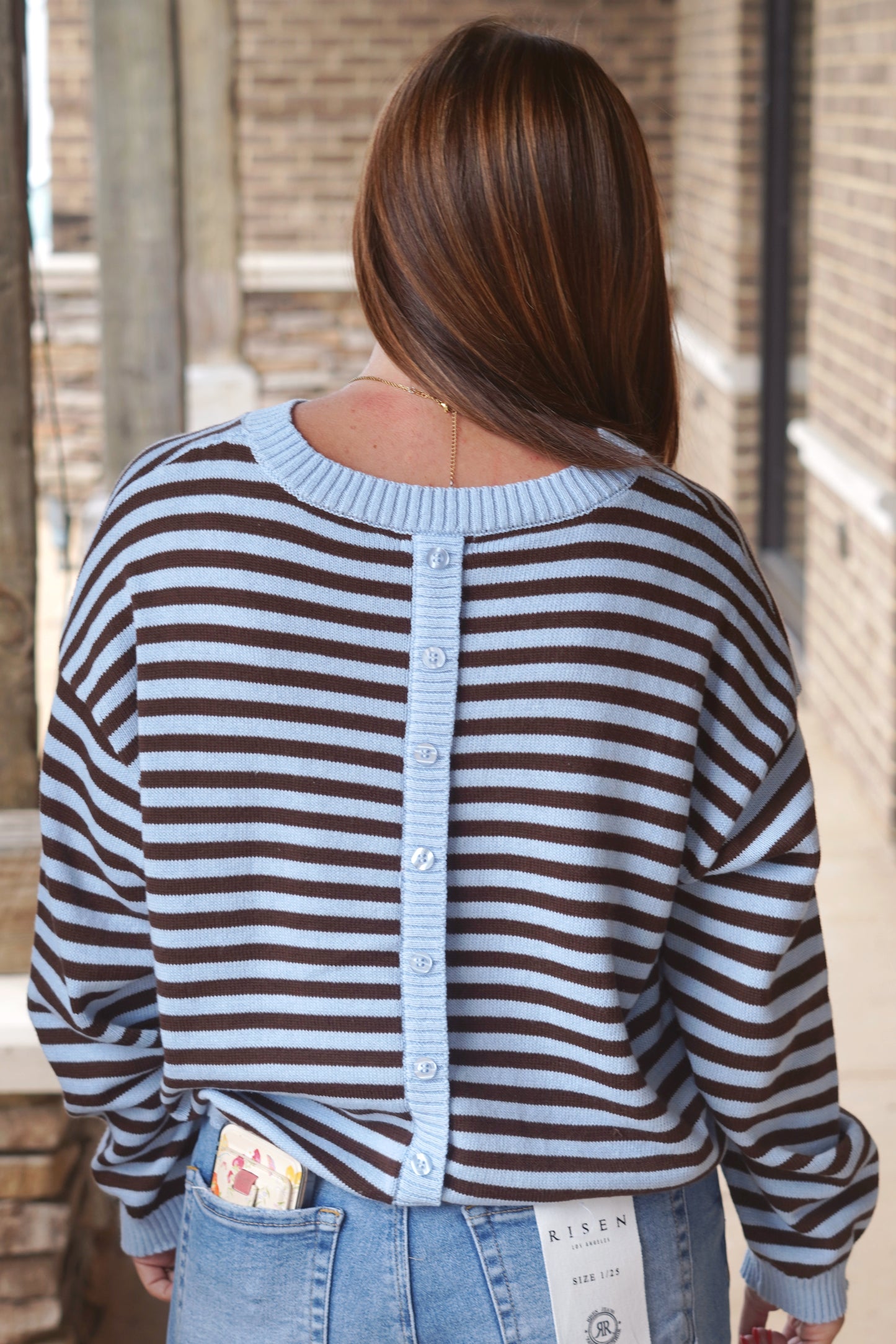 Women wearing a cream and brown striped sweater, crew neckline, with button down detailing in the back. 