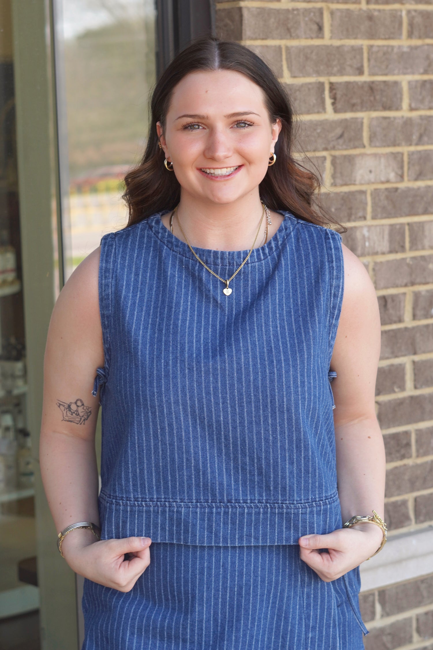 Women wearing a denim top with white pinstripe, round neckline, sleeveless with side ties. 