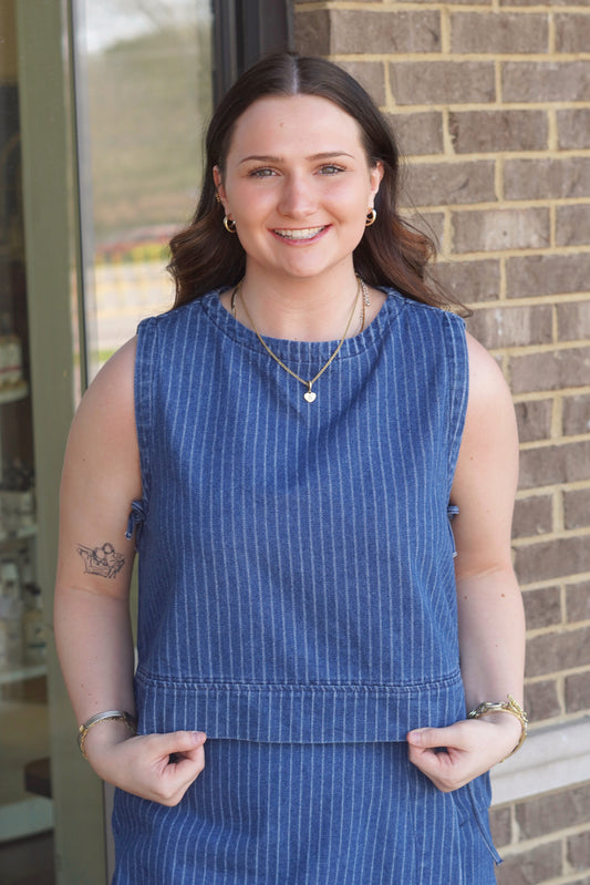 Women wearing a denim top with white pinstripe, round neckline, sleeveless with side ties. 