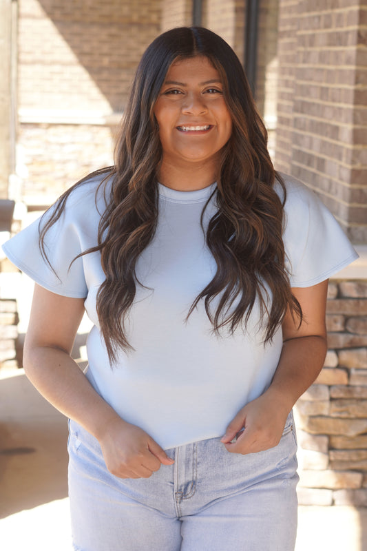 Women wearing a sky blue top with flutter sleeves, and a round neckline. 