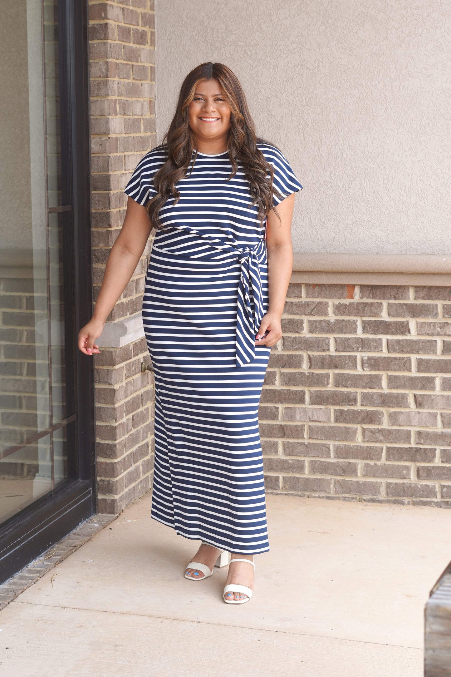 Women Wearing a Navy and White Striped Maxi Dress, Round Neckline, Tie-Waist Detail, Short Sleeve. 