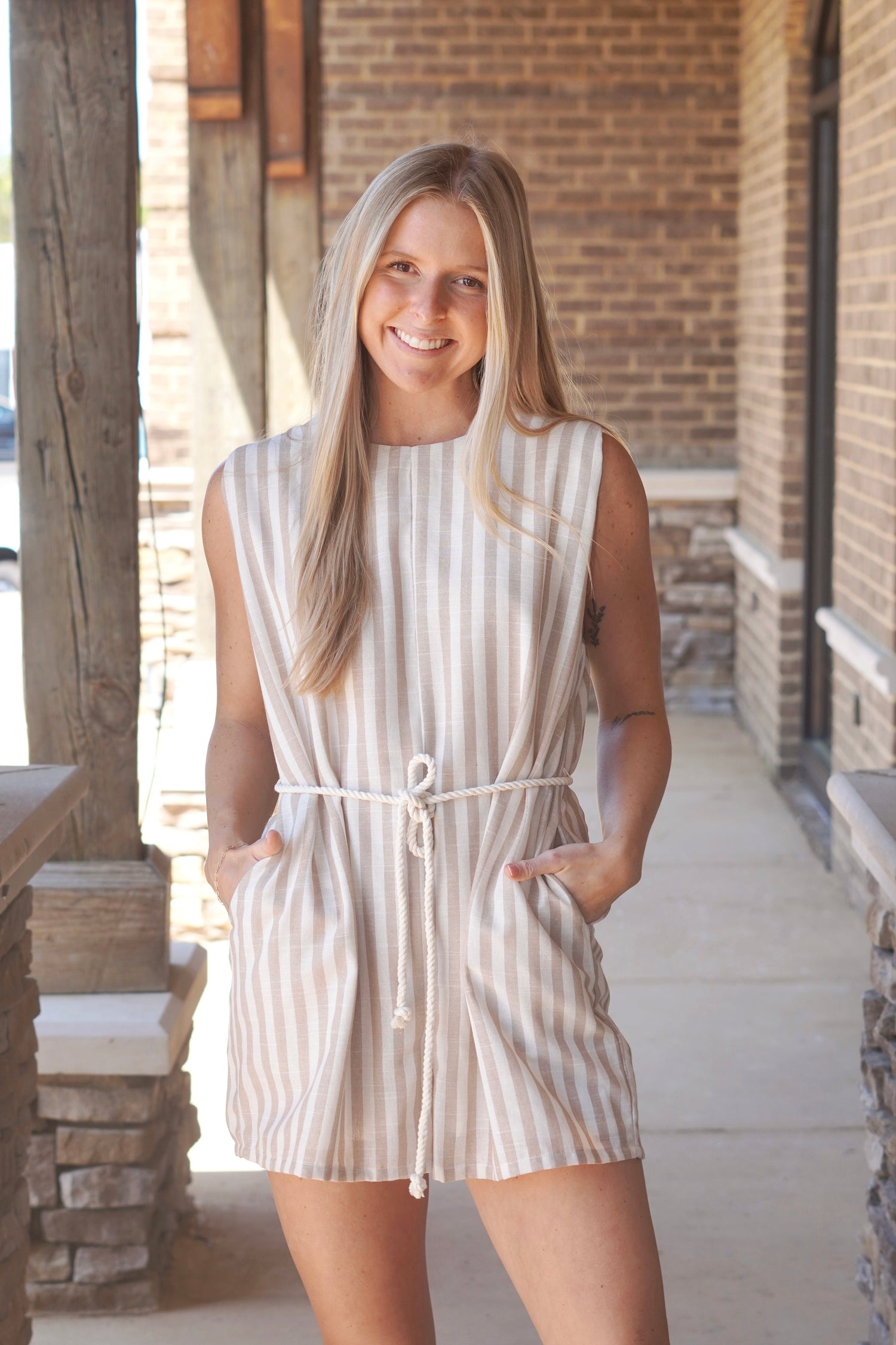 Women wearing a tan striped romper, sleeveless,  with a rope belt. 