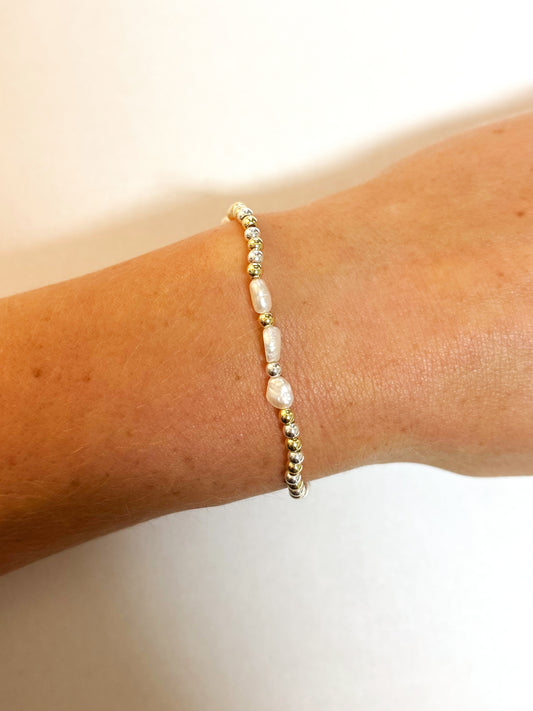 Bracelet with pearls, sliver and gold accents on a wrist against a neutral background