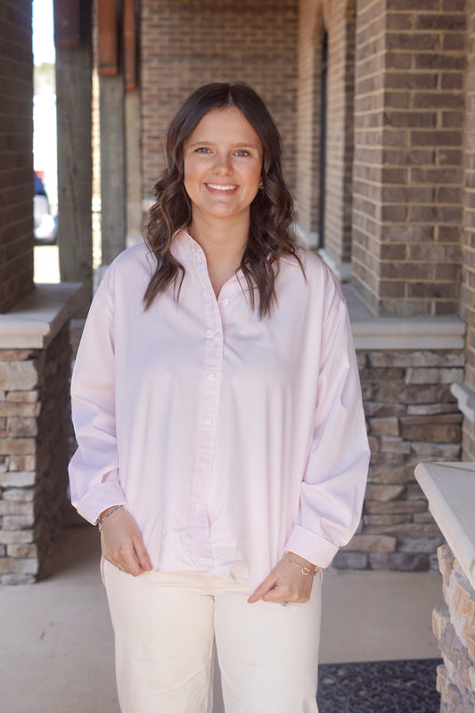 Women wearing a light pink long sleeve button up top, paired with some white pants. 