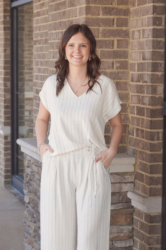 Women wearing a short sleeve ivory top with thin black stripes, v neckline, flowy fitted, paired with the match pants